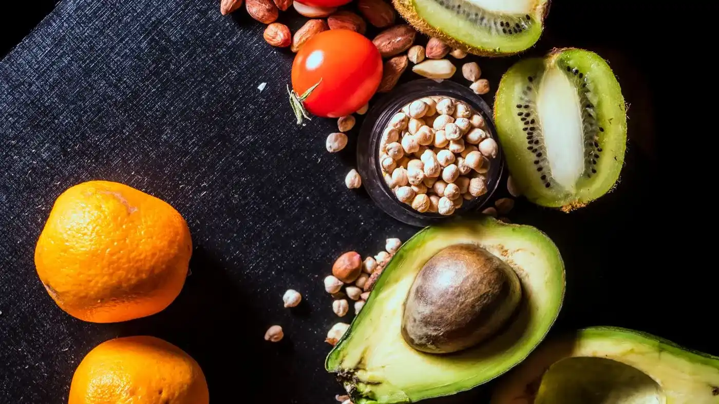 Naranjas, aguacate partido, kiwi, manzana roja, tomates y almendras sobre una tela negra: alimentos para la guía de alimentos para la erección