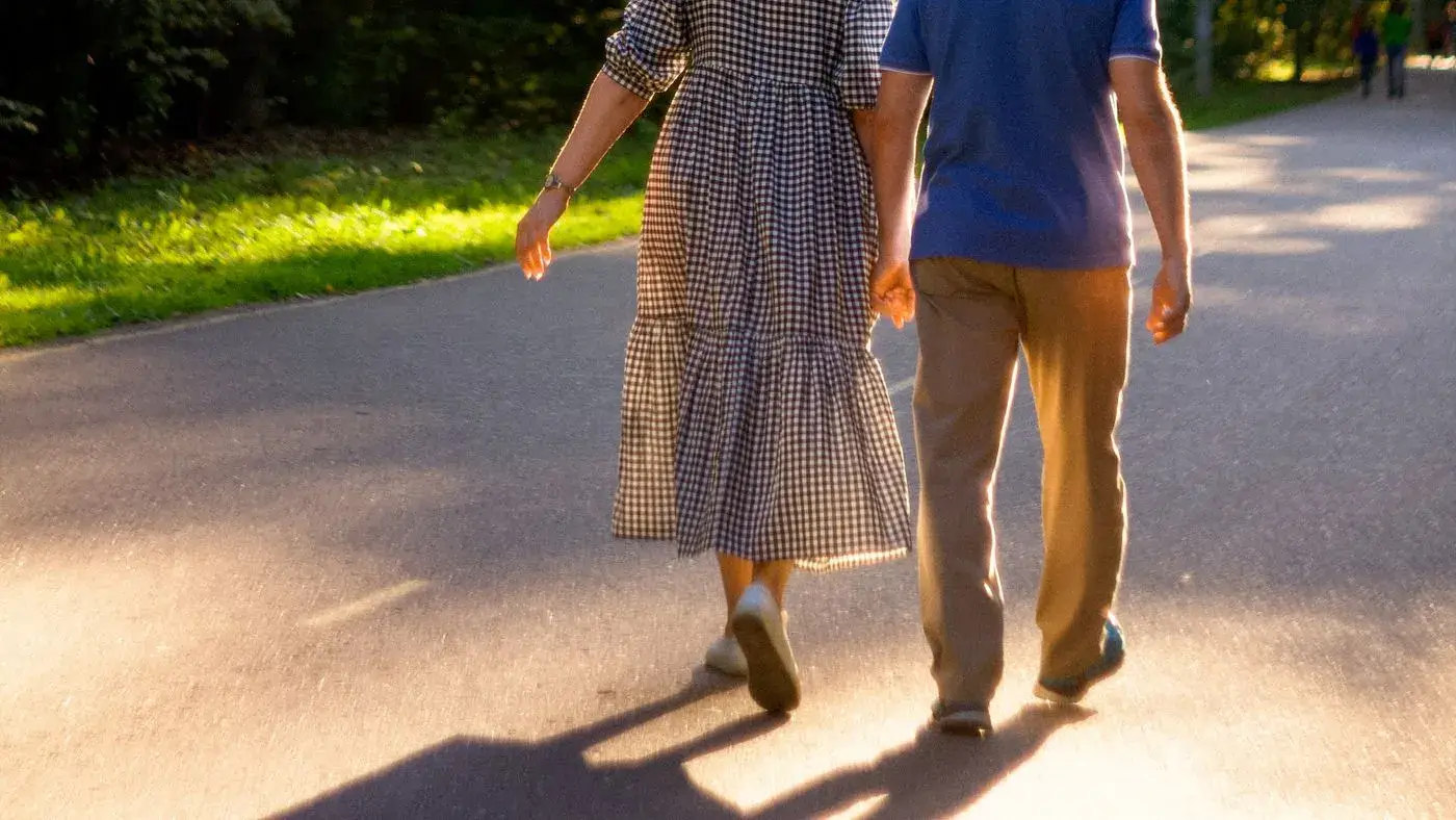Pareja de mediana edad caminando de la mano por una calle arbolada al atardecer, vista de espaldas: imagen para la guía de cómo aumentar la libido