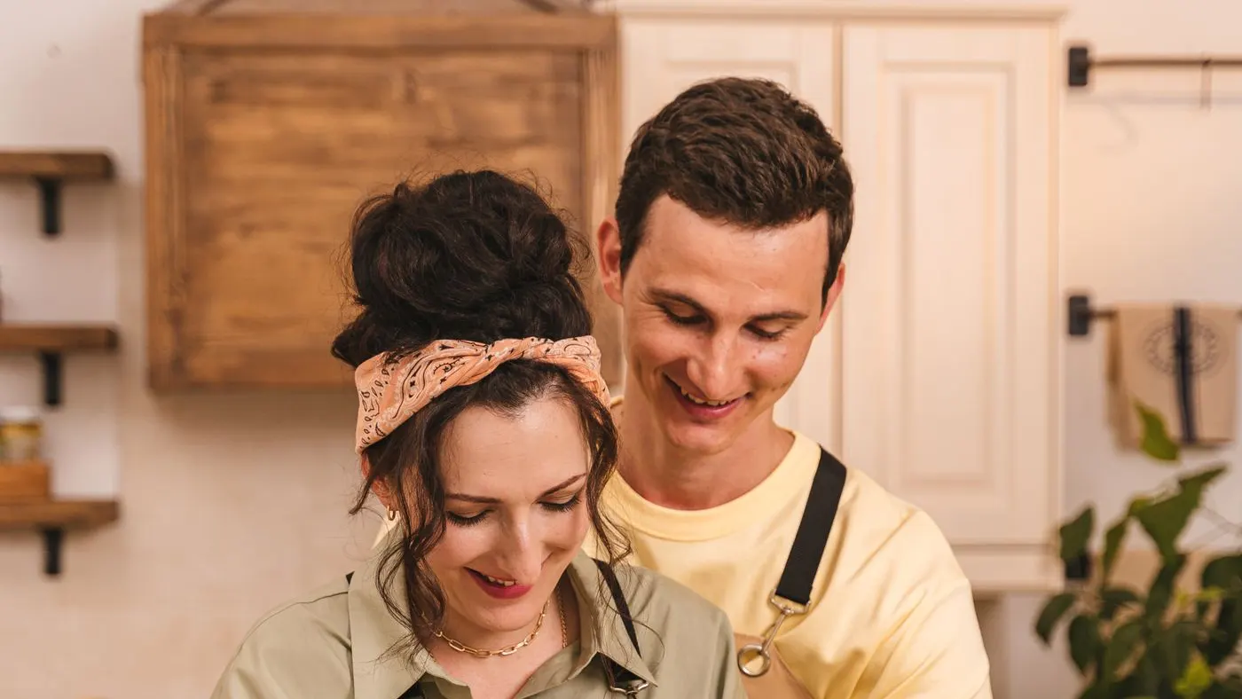 Pareja cocinando junto en una cocina luminosa, él abraza a ella por detrás mientras amasan sobre una tabla de madera: imagen para la guía sobre la libido
