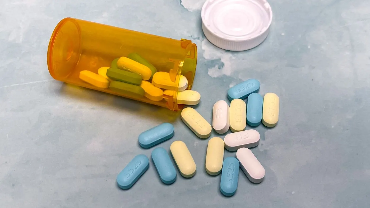 Frasco naranja de pastillas volcado sobre una superficie azul grisácea, con pastillas alargadas de colores y la tapa blanca al lado: imagen para la guía de pastillas para la eyaculación precoz