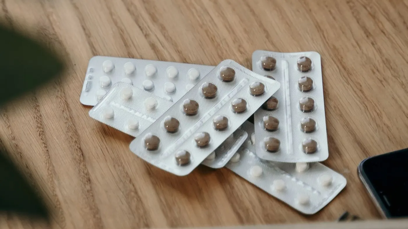 Varias tiras de pastillas redondas sobre una mesa de madera junto a un cuaderno abierto y un teléfono: imagen para la guía del vardenafil